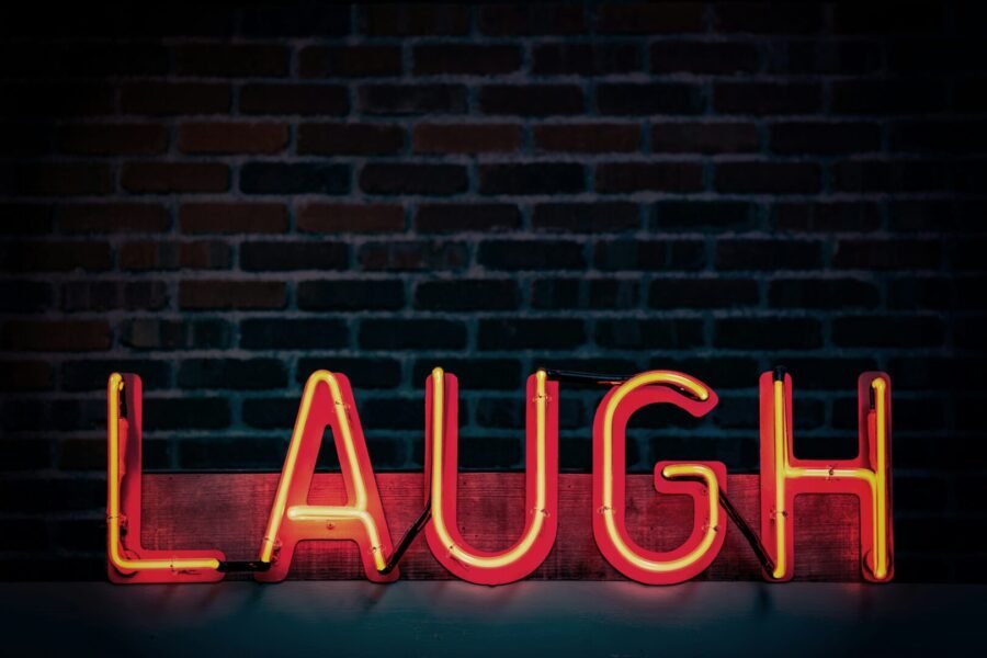 Image of a neon sign which reads 'laugh', against a brick wall background.